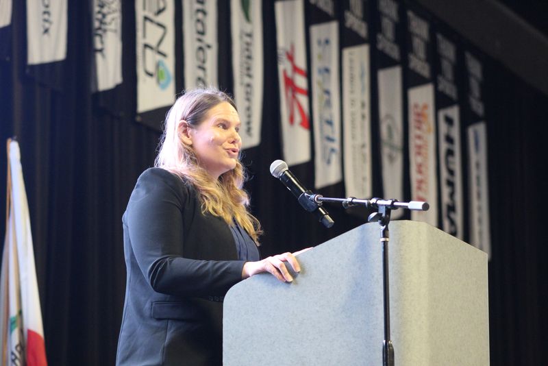 Dr. M. Anne Visser speaking at the podium in front of the sponsor banners