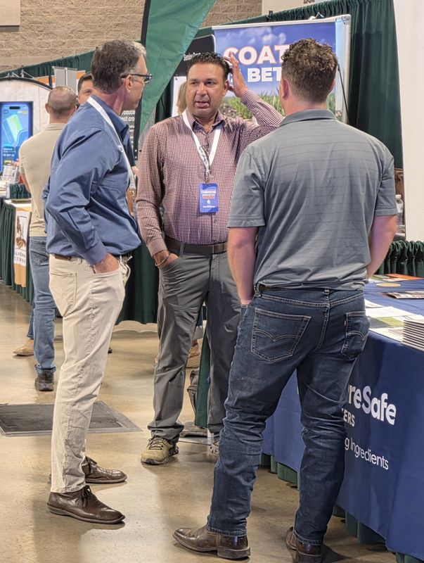 Three attendees talking near a booth on Day 2