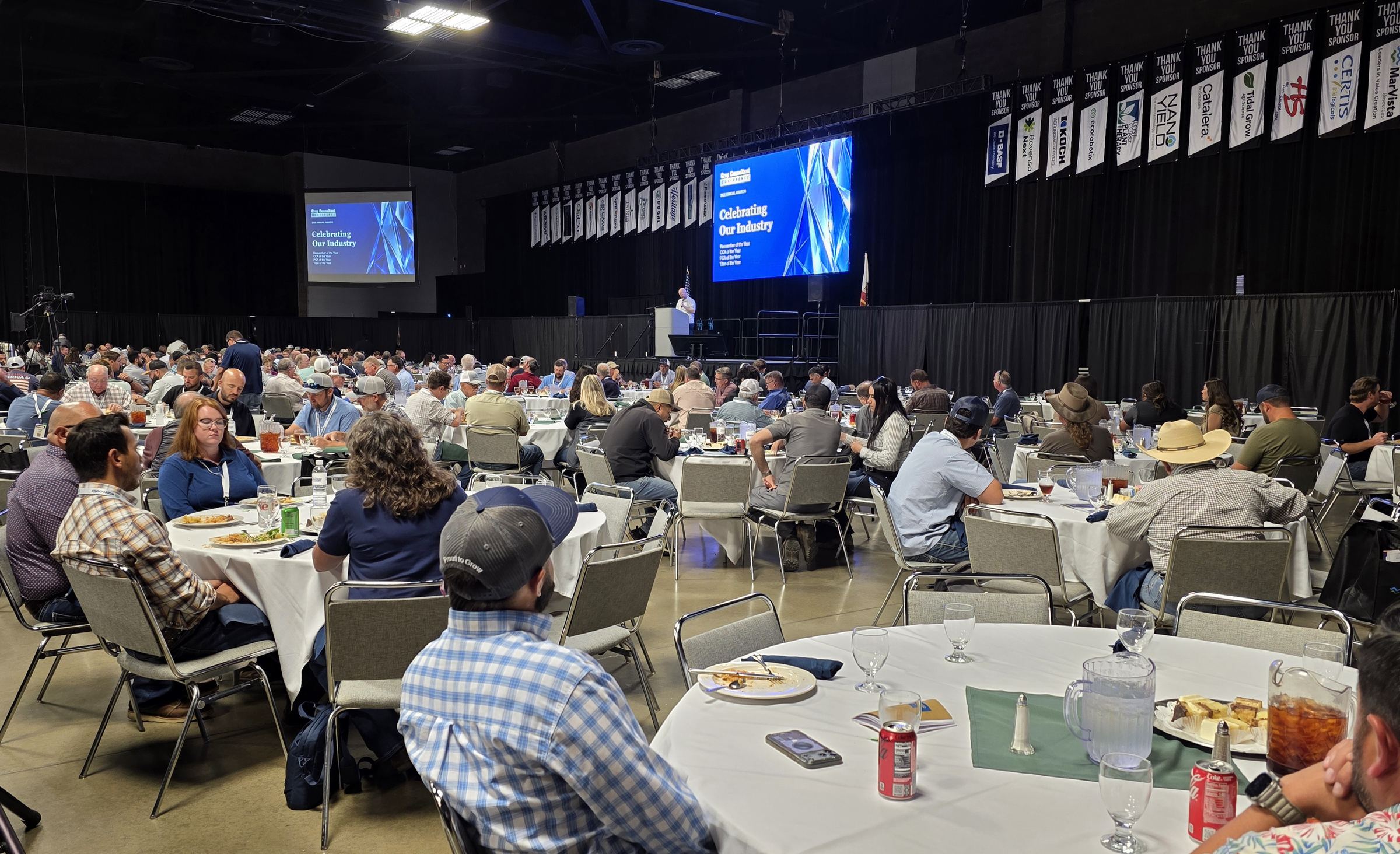 A full Expo Hall at the Day 2 awards luncheon, with Celebrating Our Industry on the big screen and thank-you banners for every sponsor overhead