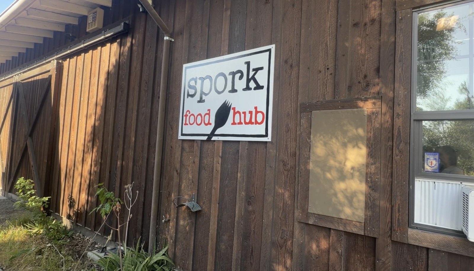 A sign reading "spork food hub" mounted on the wood-sided exterior of Spork Food Hub in Davis, California