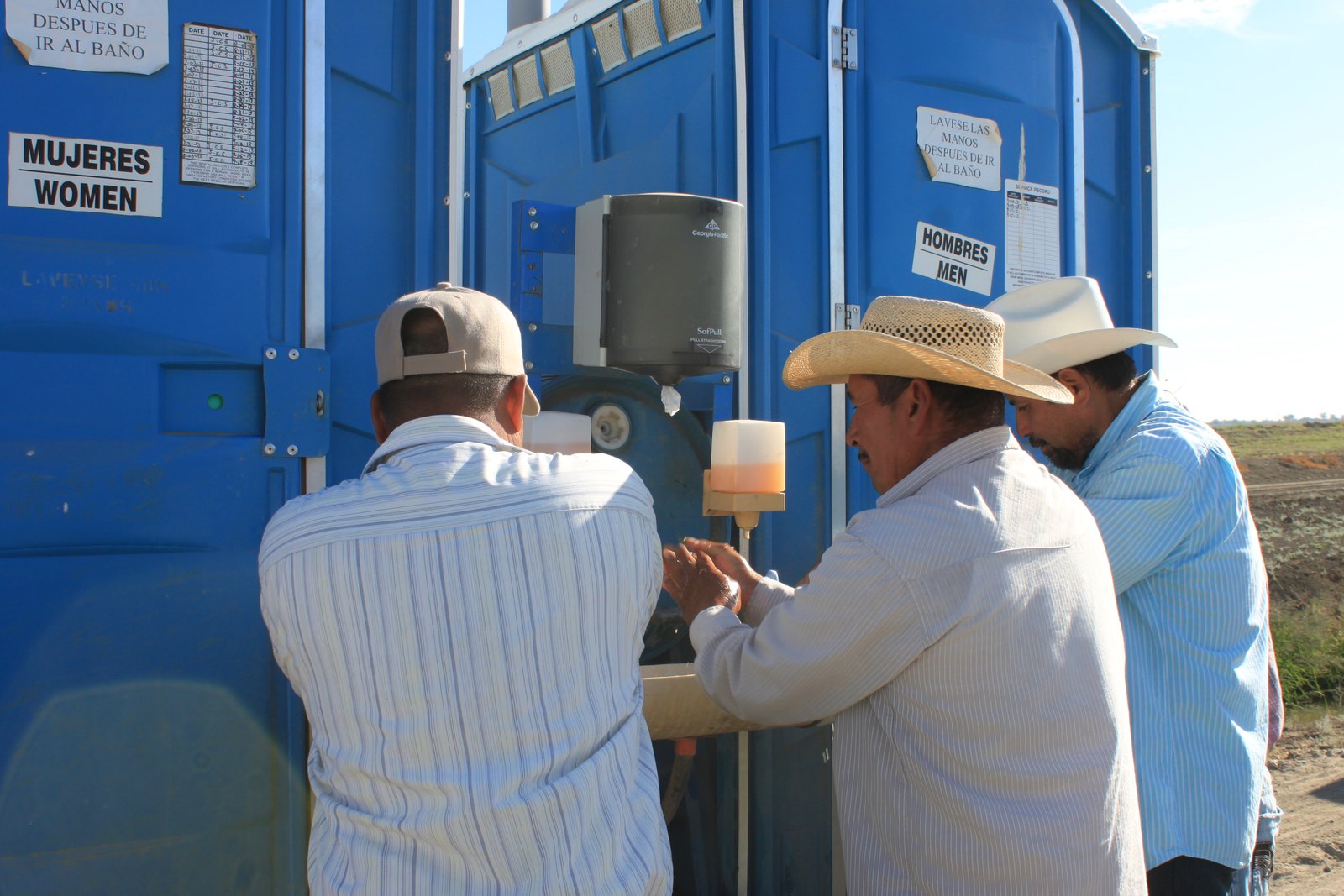 Farmworkers wash their hands at a portable field sanitation station marked with bilingual women's and men's signs in a California field